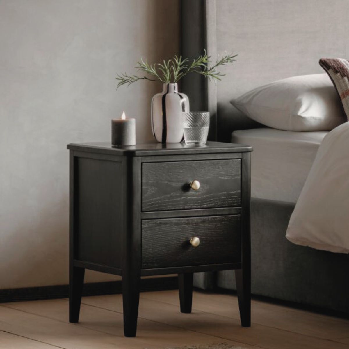 Alvar Black Two Drawer Bedside Table with gold handles and raised base — modern black bedroom furniture by Mallet & Plane.