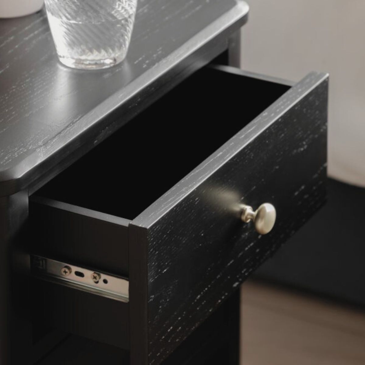 Alvar Black Two Drawer Bedside Table with gold handles and raised base — modern black bedroom furniture by Mallet & Plane.